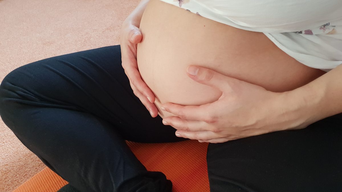 Eine schwangere Frau sitzt auf einer Yogamatte im Schneidersitz