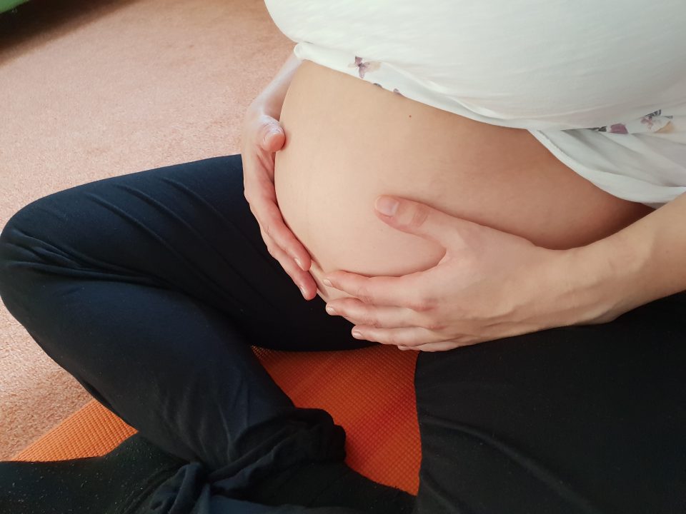 Eine schwangere Frau sitzt auf einer Yogamatte im Schneidersitz