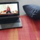 Auf einer roten Yogamatte sthet ein Laptop, auf dem Bildschirm ist ein Video mit Marion im Schneidersitz zu sehen