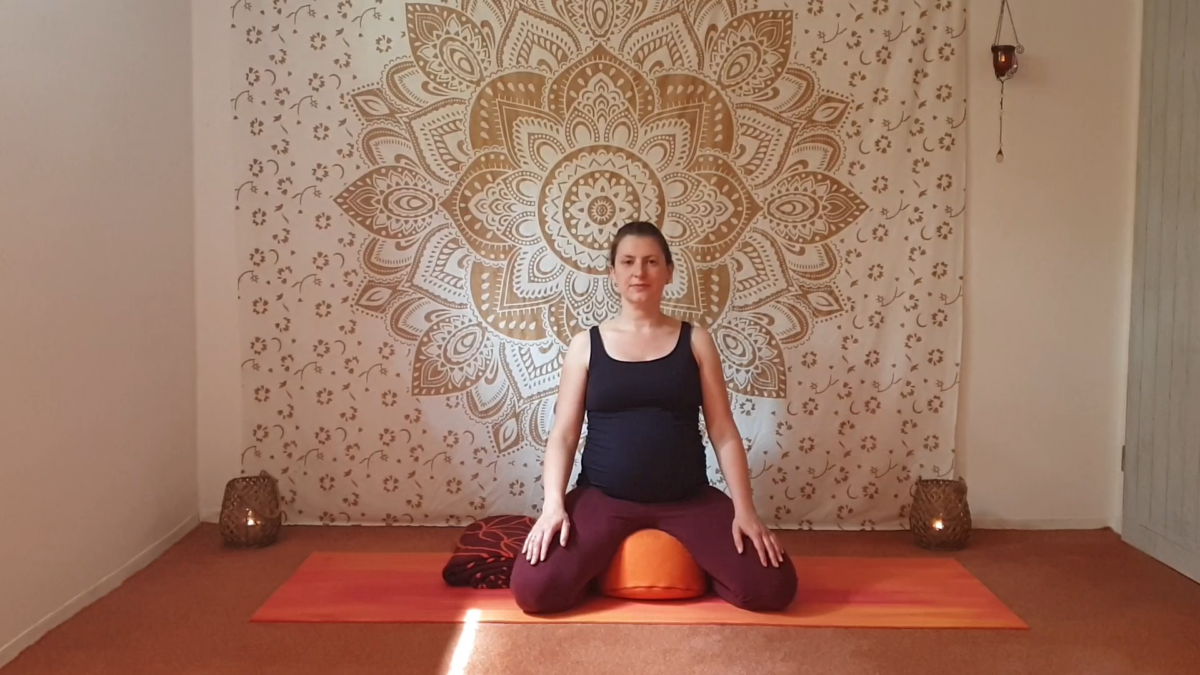 Marion sitzt schwanger im Versensitz auf dem Yogakissen.mit