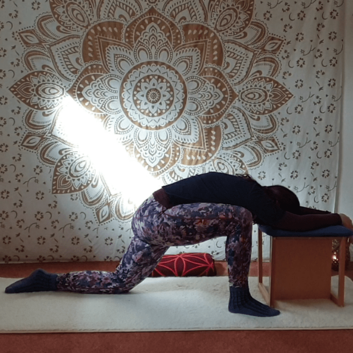 Marion übt Yin Yoga und die Position der Drache. Marion kniet auf der Matte, das rechte Bein ist vorn aufgestellt. Der Oberkörper ruht auf einem Hocker.