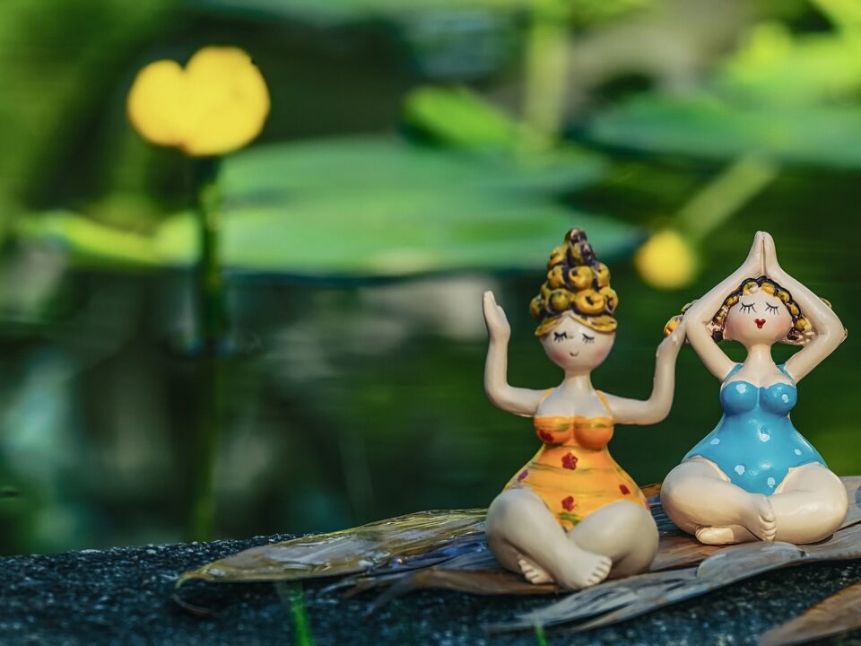 Zu sehen sind zwei bunte Porzellanfiguren in unterschiedlichen Yogapositionen